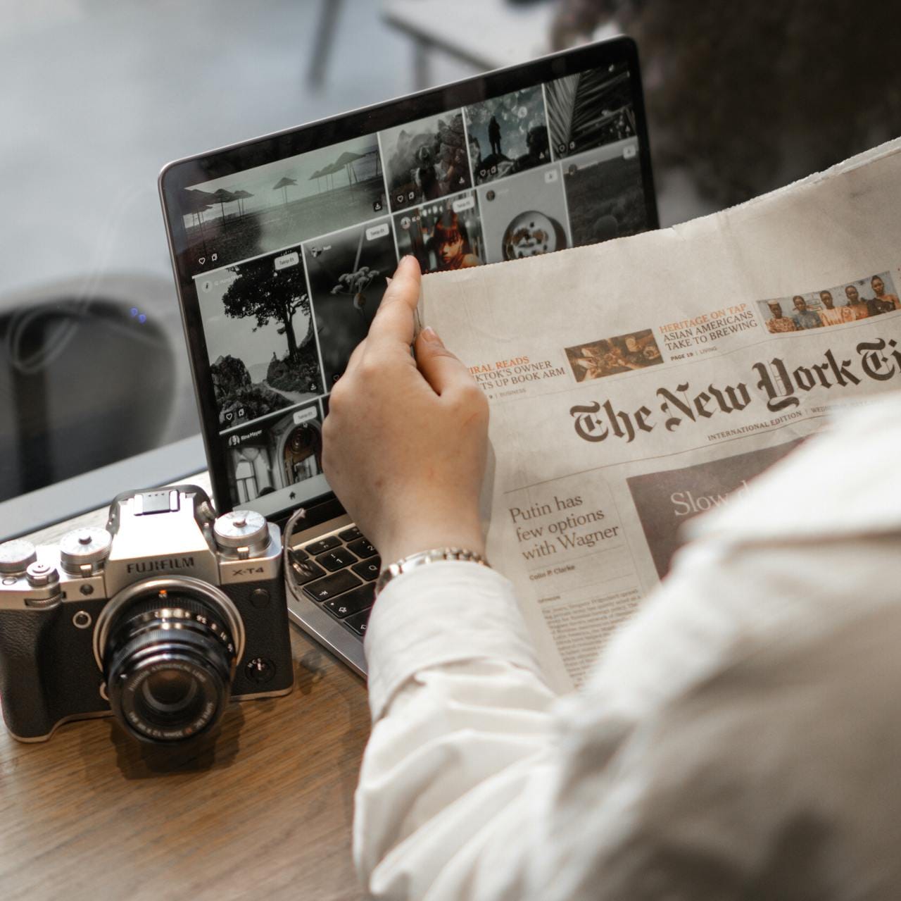 Offerings Close-up of a person reading The New York Times by a laptop and camera.